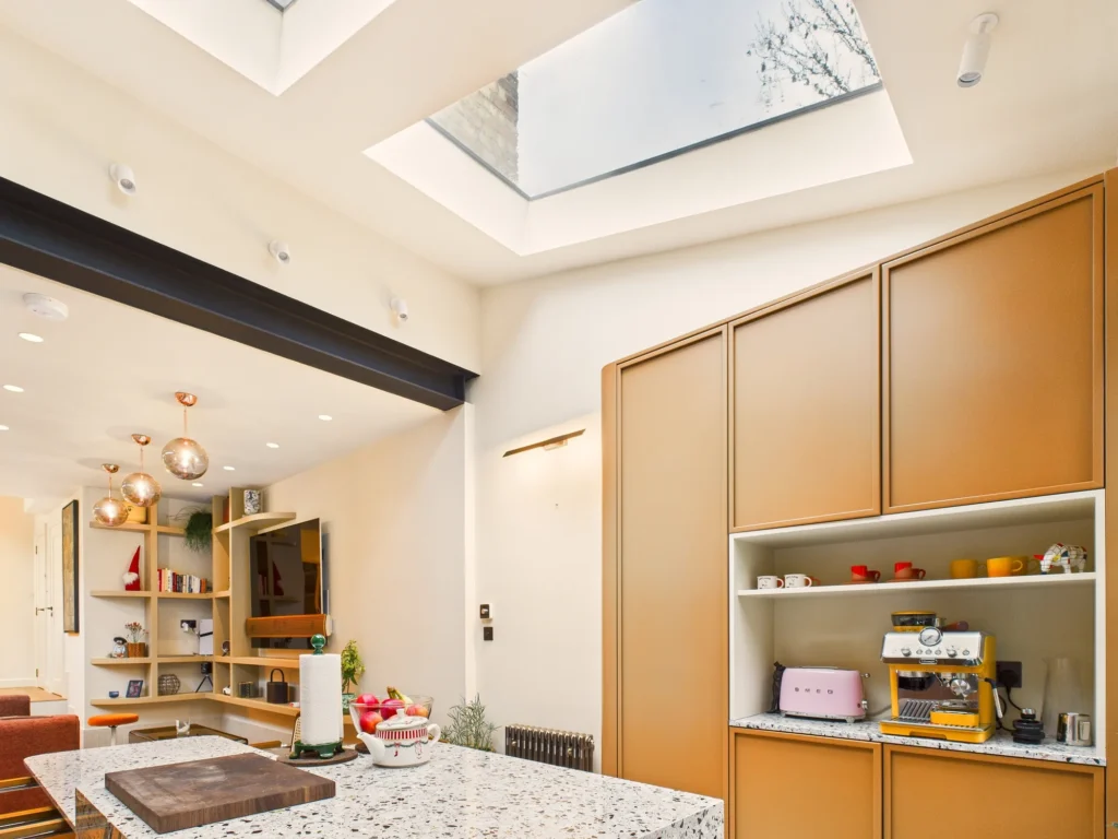 Large flat rooflights above the kitchen with mustard yellow tall cabinets and a terrazzo island