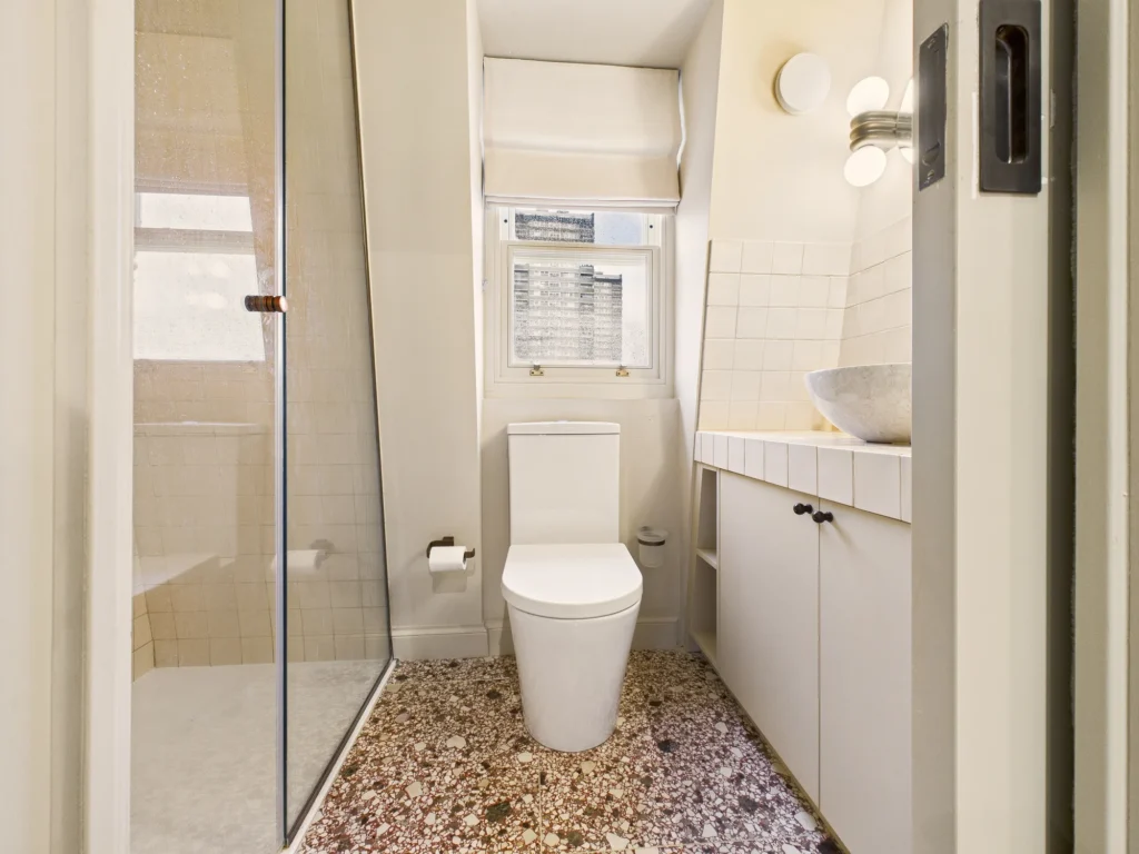 Ensuite shower room in the mansard loft with a terrazzo floor, tiled vanity top, stone basin and sash window