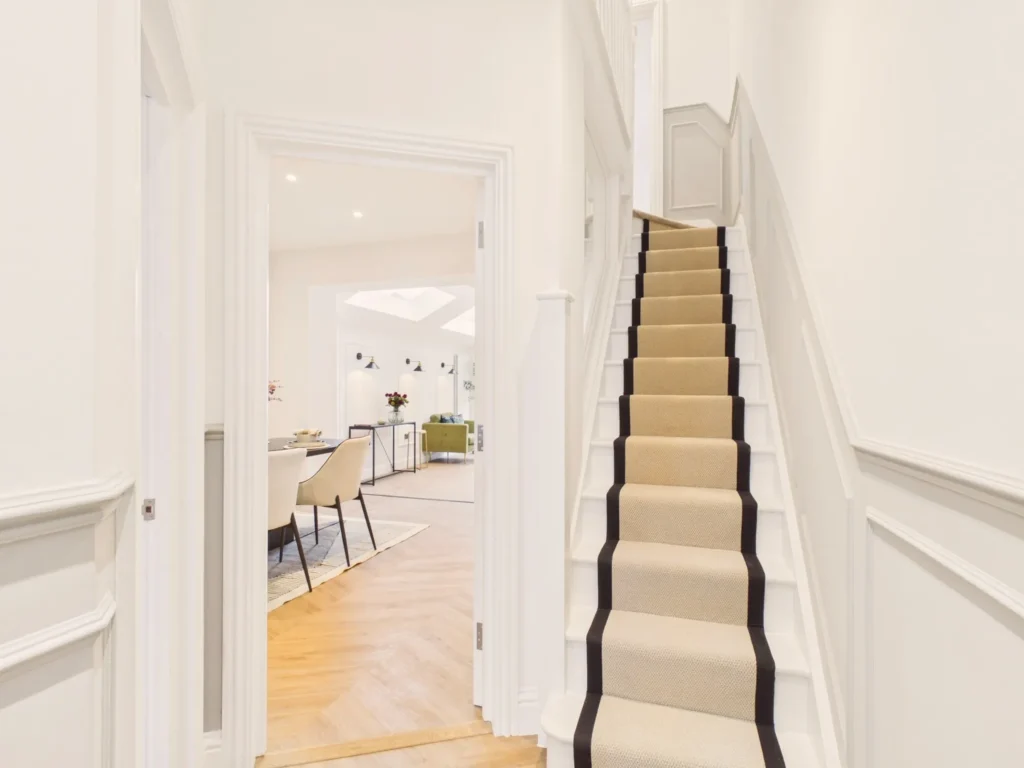 Entrance hall with wall panelling and a white staircase with a black-edged runner, looking through to the dining room and rooflights