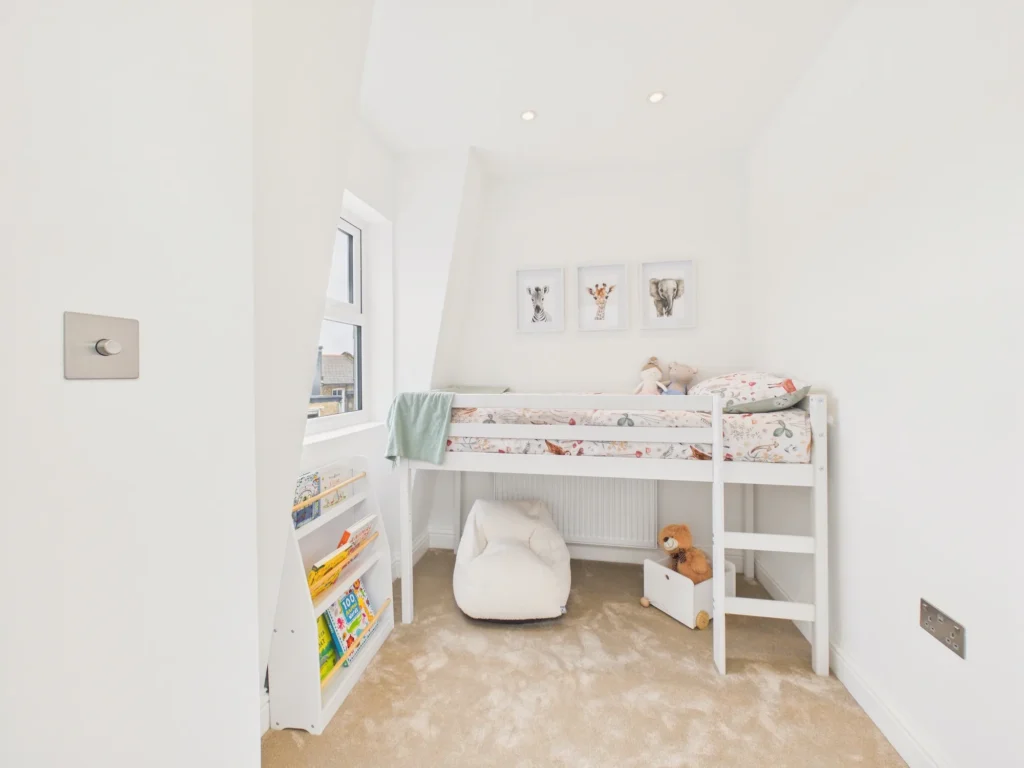Child's bedroom in the mansard loft with a cabin bed, a window set in the sloping mansard wall and a book rack