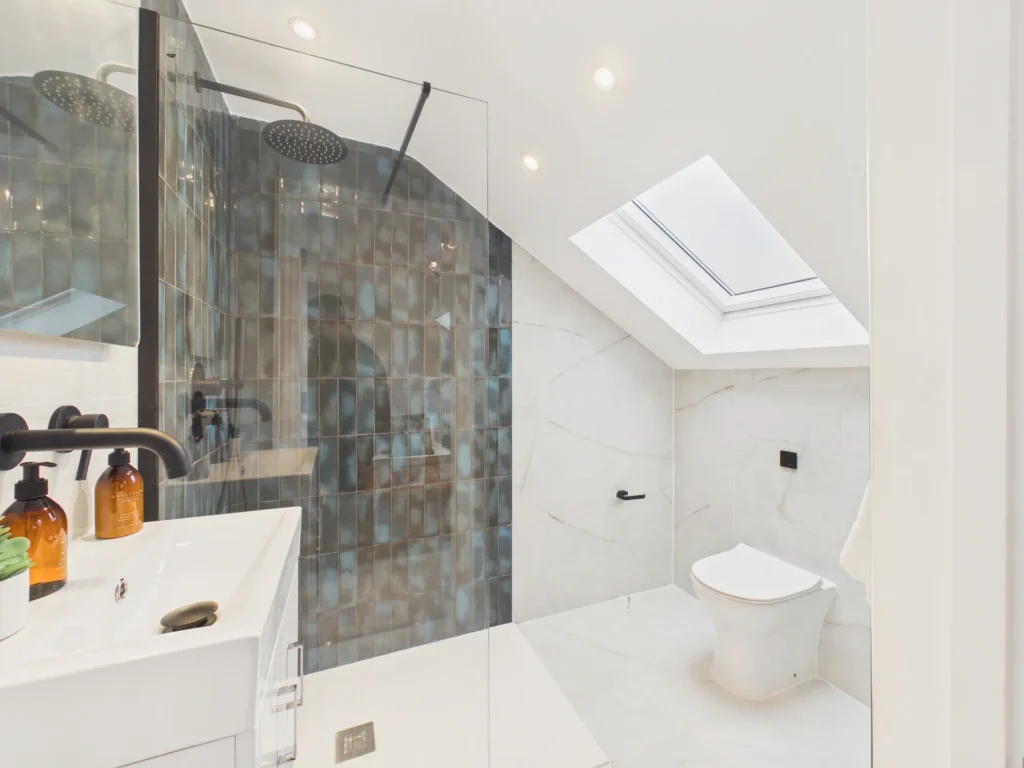 Loft ensuite with a walk-in shower in glazed teal tiles, marble-effect walls, matt black fittings and a rooflight