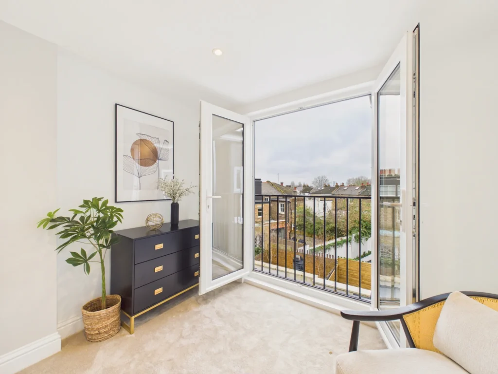 French doors open onto a Juliet balcony with black metal railings and views over the gardens and rooftops of Kensal Rise