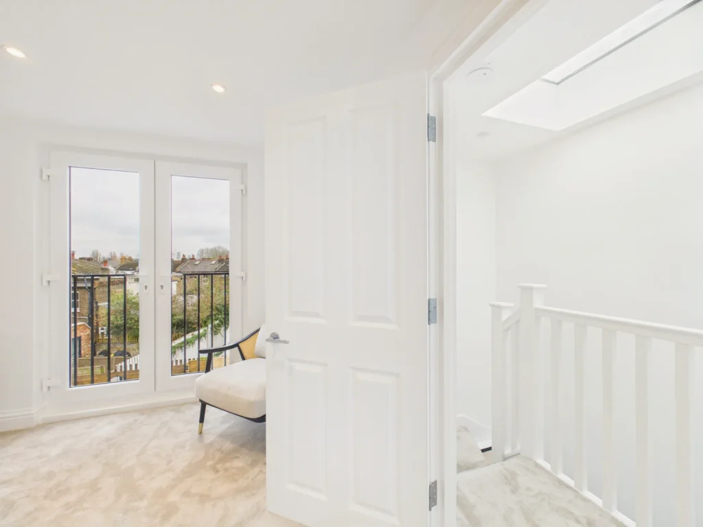 Loft master suite seen from the landing, with French doors to the Juliet balcony and the stair below