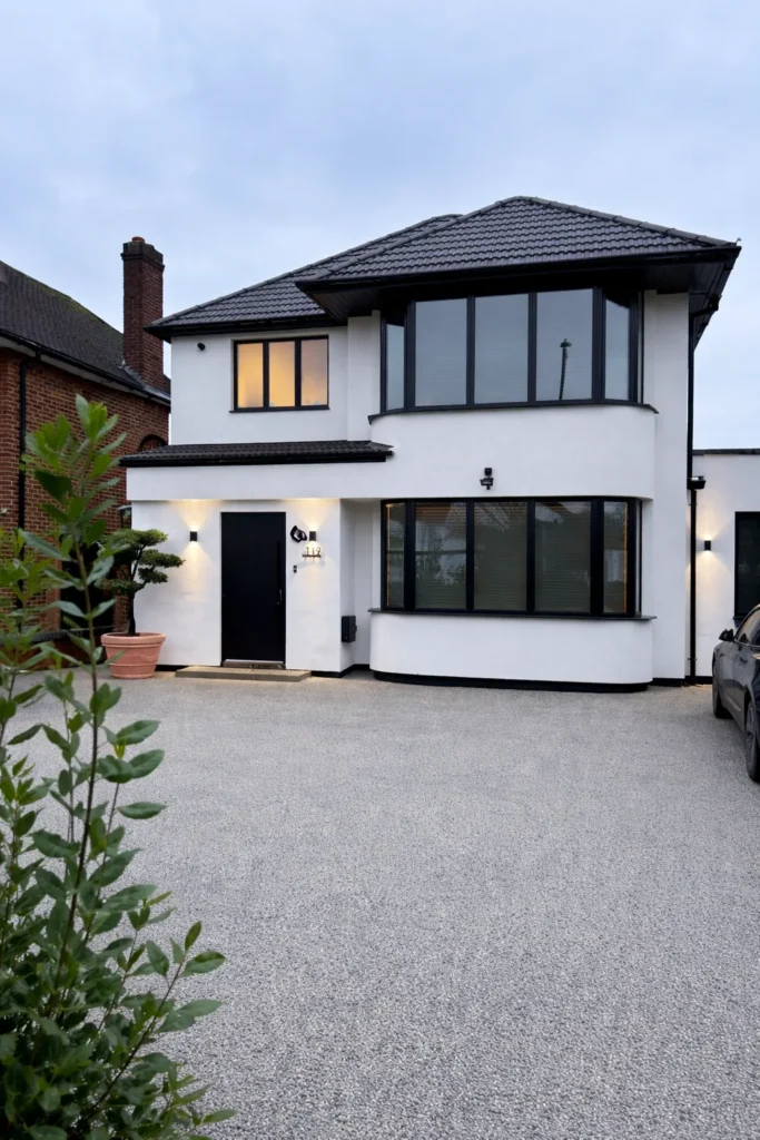 Front elevation at dusk with the curved two-storey bay in white render, black framed windows and a new dark tiled roof