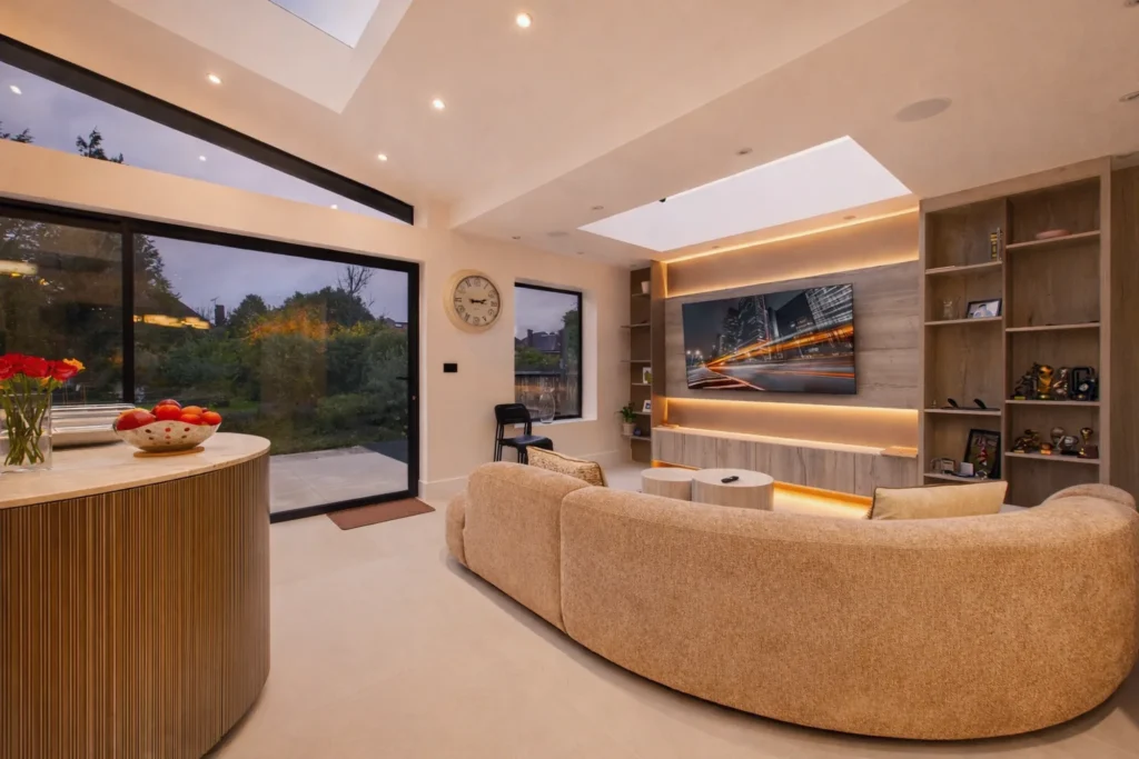 Living area in the rear wraparound extension with a curved sofa, a backlit timber media wall and sliding doors to the garden