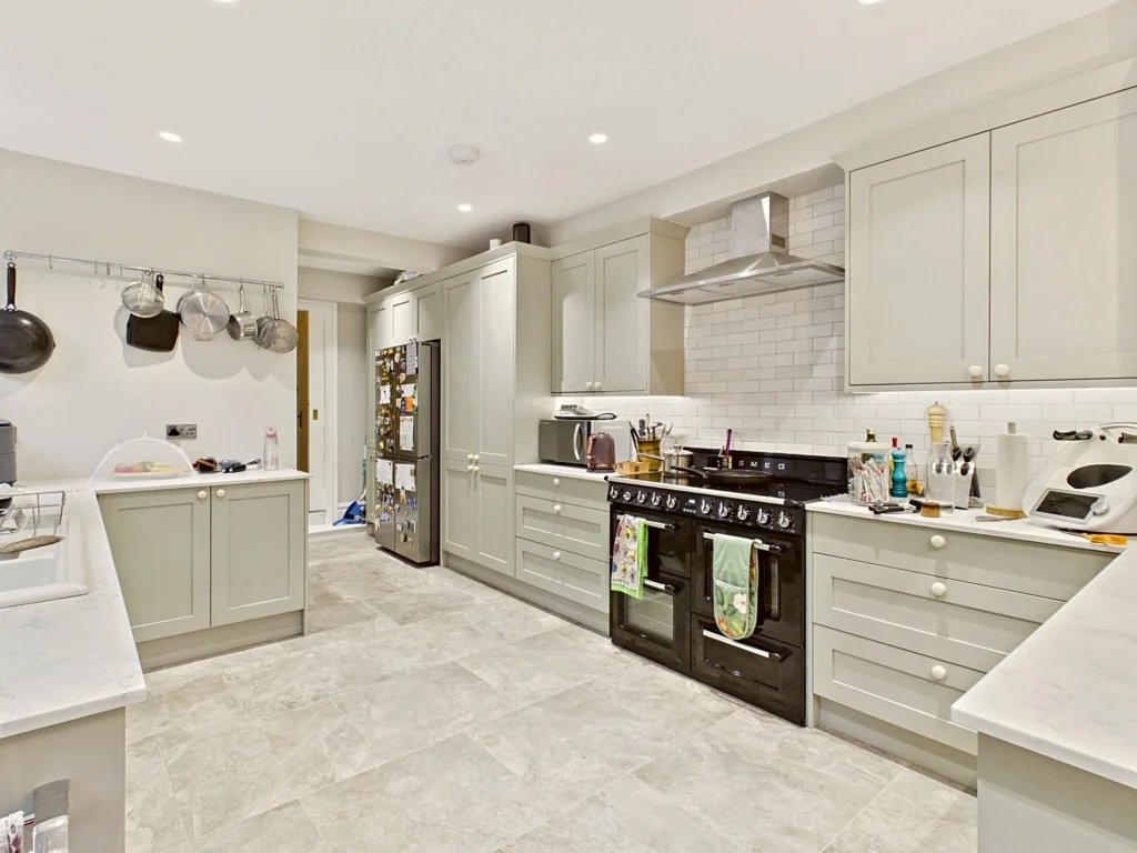 Sage green shaker kitchen with a fridge freezer set into tall housing, a black range cooker and pale stone-effect floor tiles