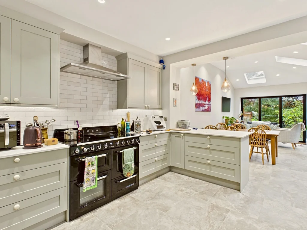 Sage green shaker kitchen with a black range cooker, metro tile splashback and a peninsula opening onto the dining area of the extension