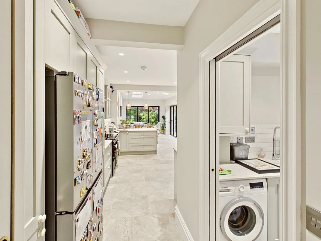 Corridor past a utility room with a washing machine, looking through the kitchen to the extension and its rear bifold doors