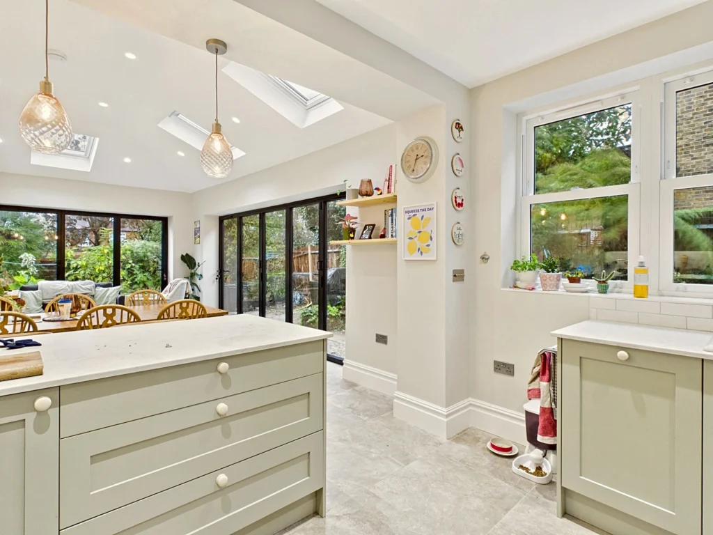 View from the kitchen island across the dining table to the lounge and bifold doors, with rooflights and glass pendant lights